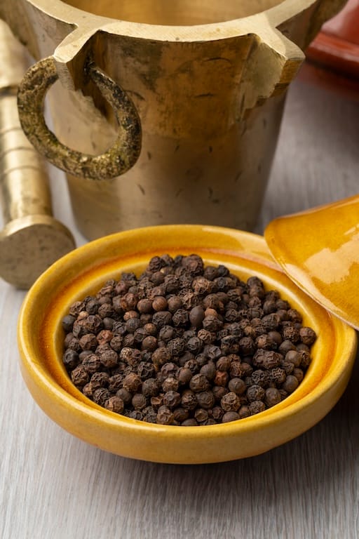 Whole black peppercorns with traditional grinder used in Aethron nanoencapsulated supplements to enhance bioavailability of active compounds