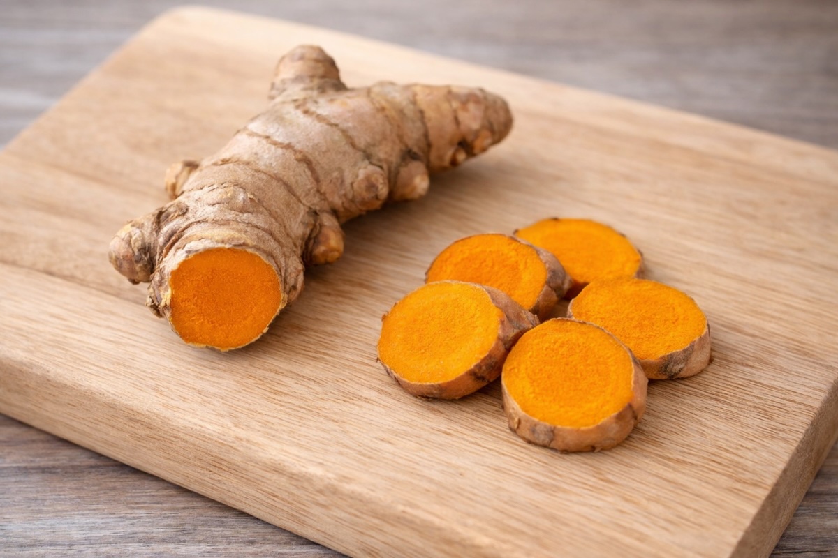 The picture shows a turmeric root and sliced turmeric on a chopping board. 